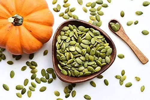 Pumpkin seeds in a bowl with a small pumpkin and wooden spoon on a white background