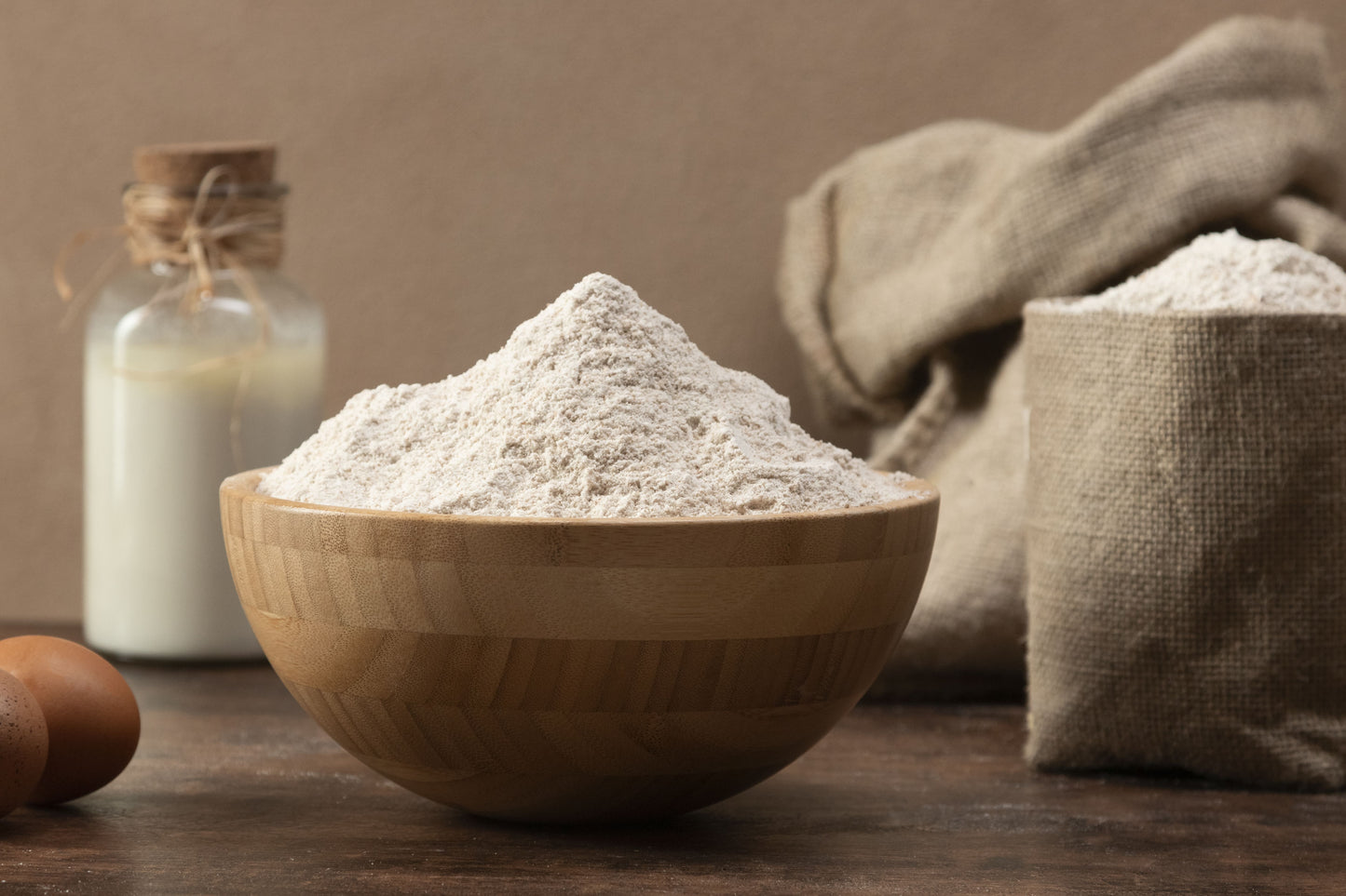Wooden bowl filled with flour on a wooden table with a brown background