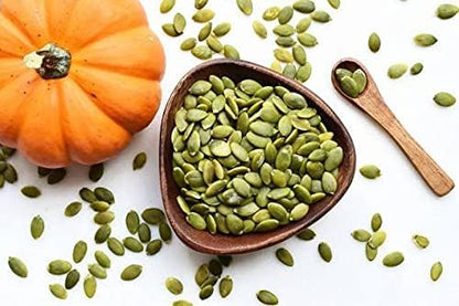 Pumpkin seeds in a bowl with a small pumpkin and wooden spoon on a white background