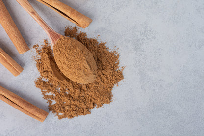 Cinnamon powder with a wooden spoon and sticks on a light gray background