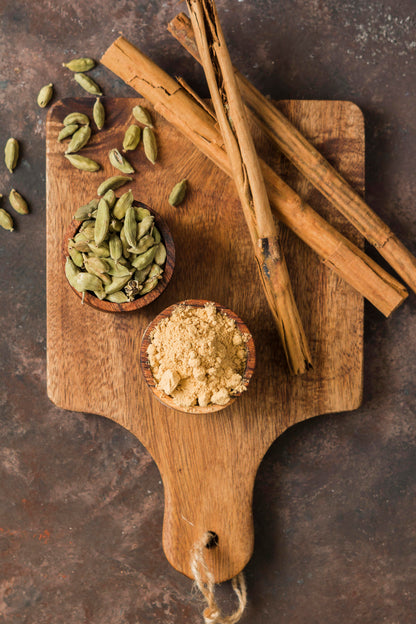 Spices including cardamom pods, cinnamon sticks, and ground spice on a wooden cutting board.