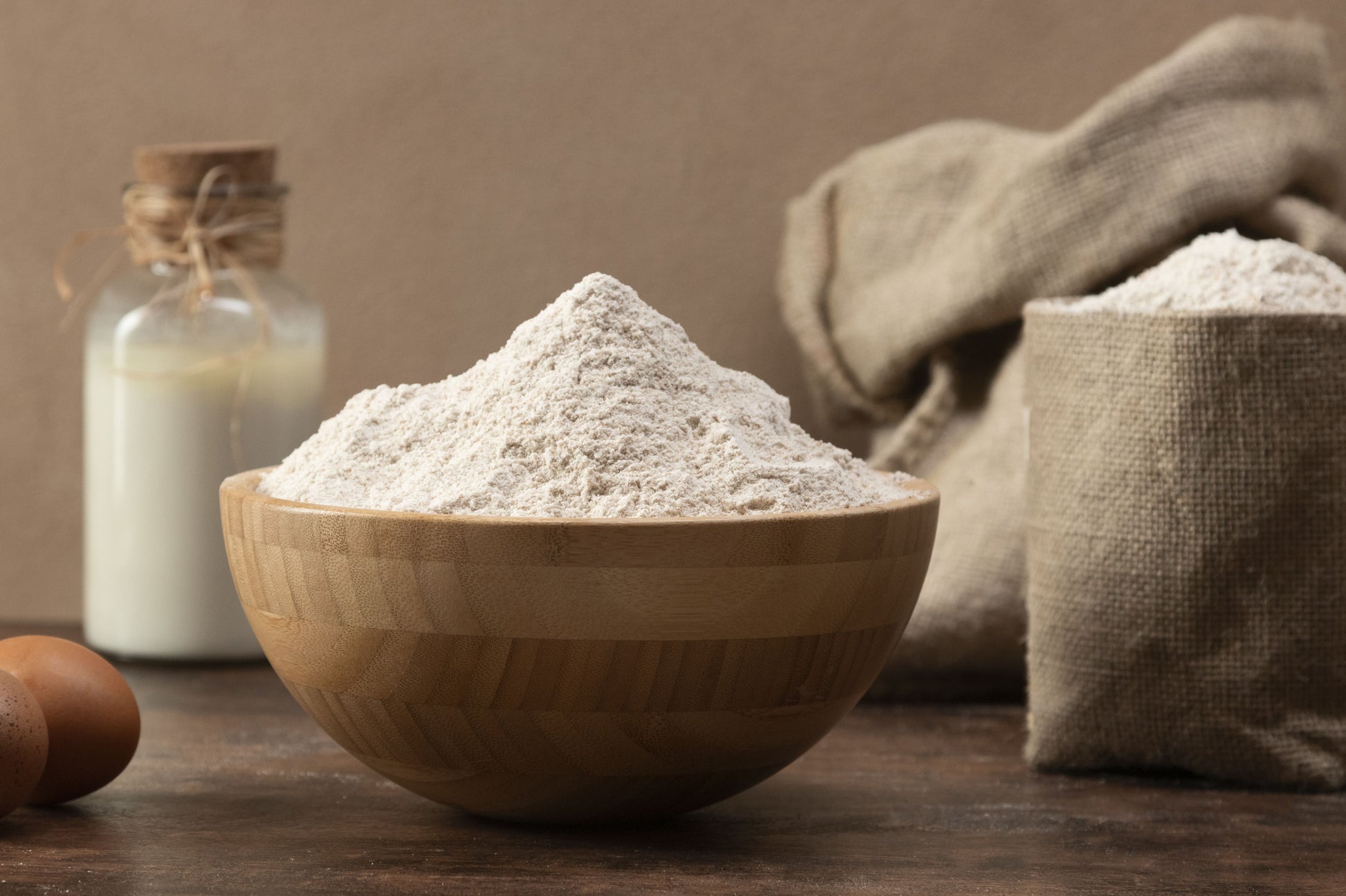 Wooden bowl filled with flour on a wooden table with a brown background